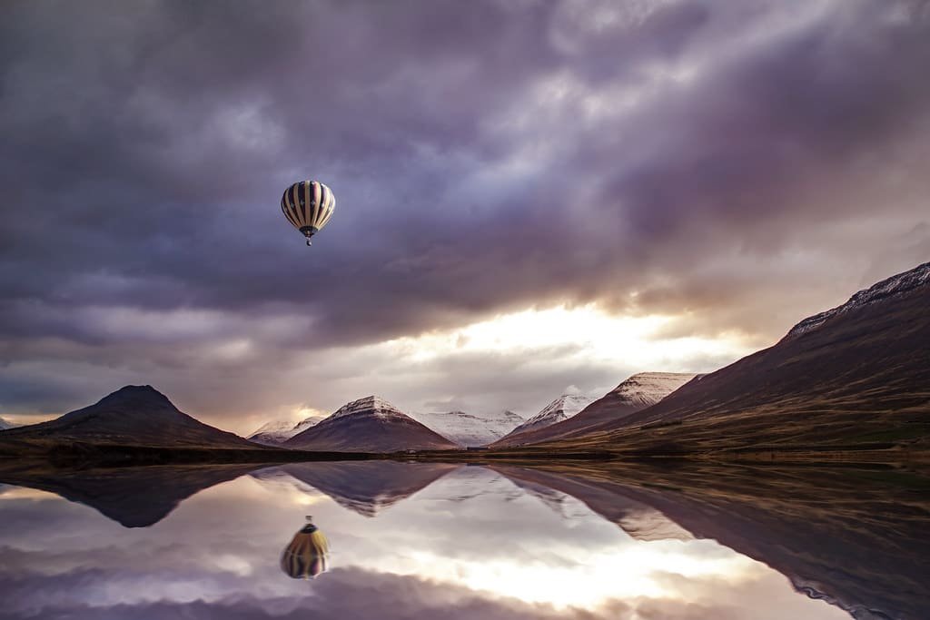 A hot-air balloon drifting above a still lake ringed by mountains