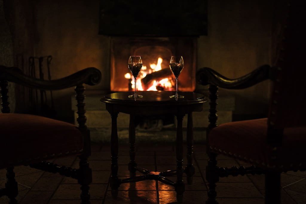 Two armchairs drawn up to a lit open fire in a dark panelled room