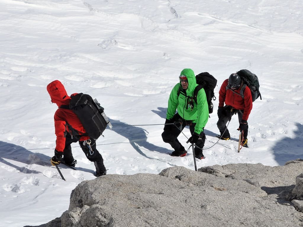 A roped party of three climbers moving together on snow