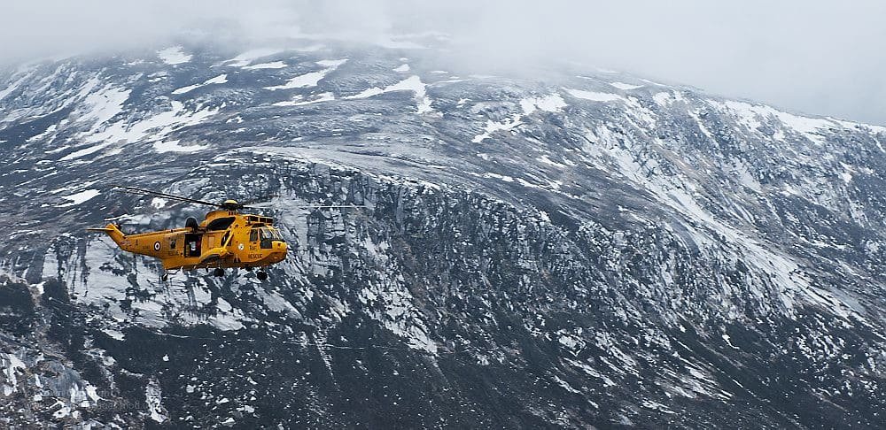 A helicopter flying low over a crevassed glacier