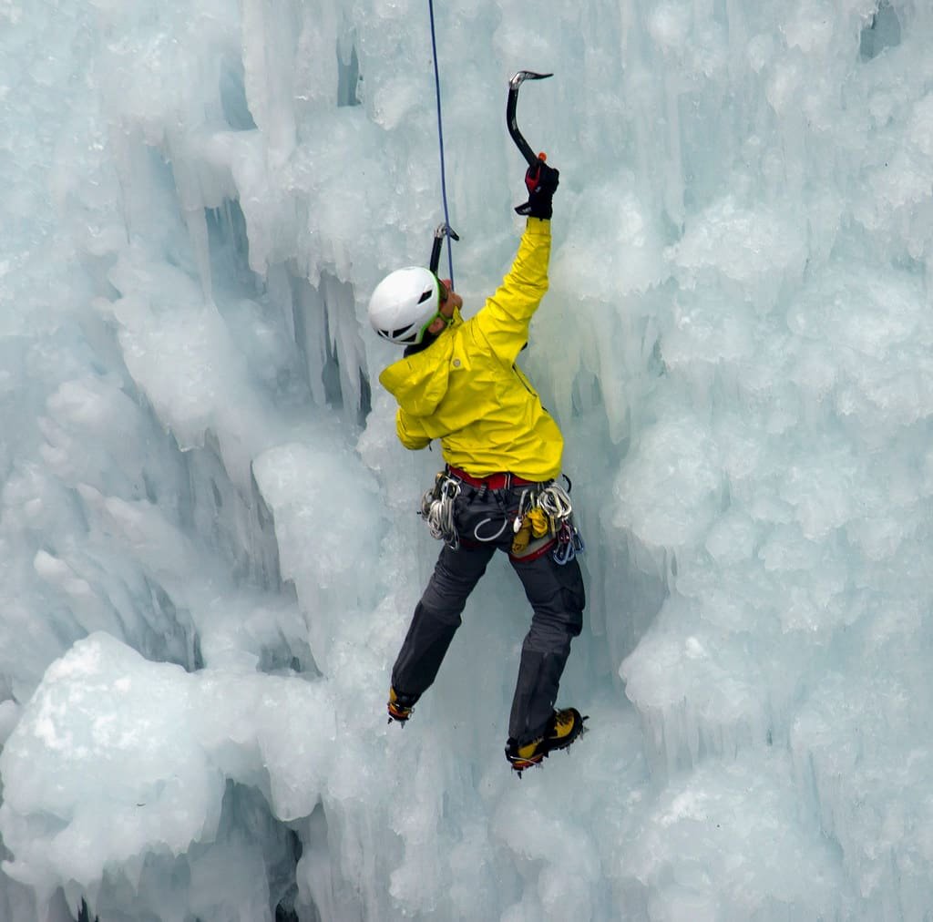 An ice climber swinging a tool into a frozen blue waterfall