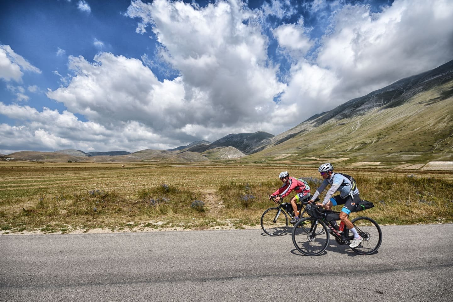 Road cyclists climbing an open mountain pass under big clouds