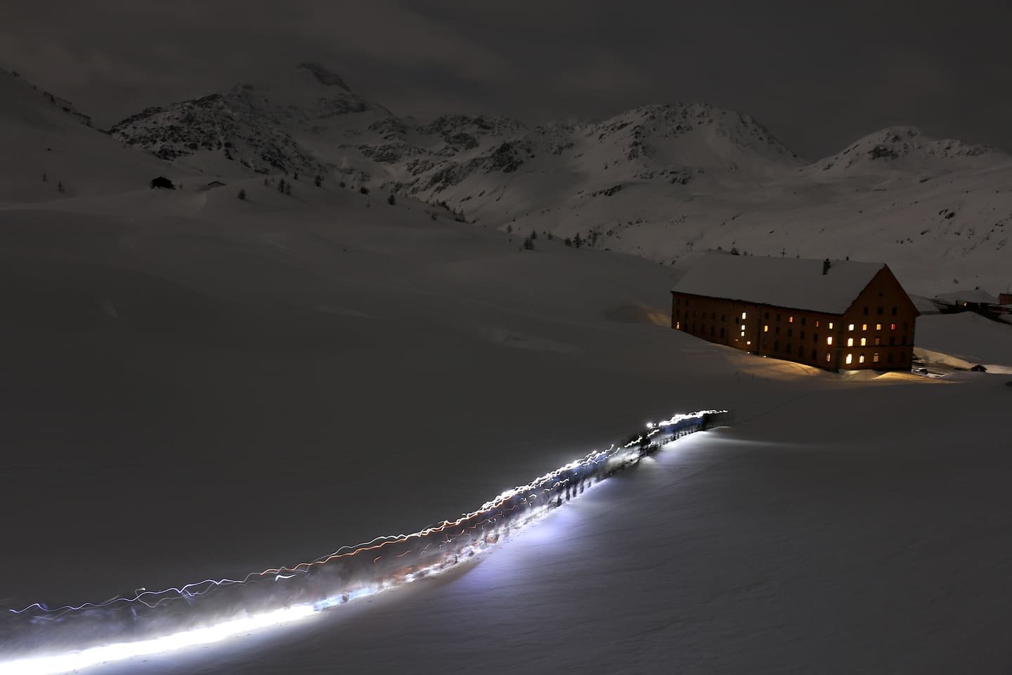 A lit mountain hut at night above a torchlit skin track
