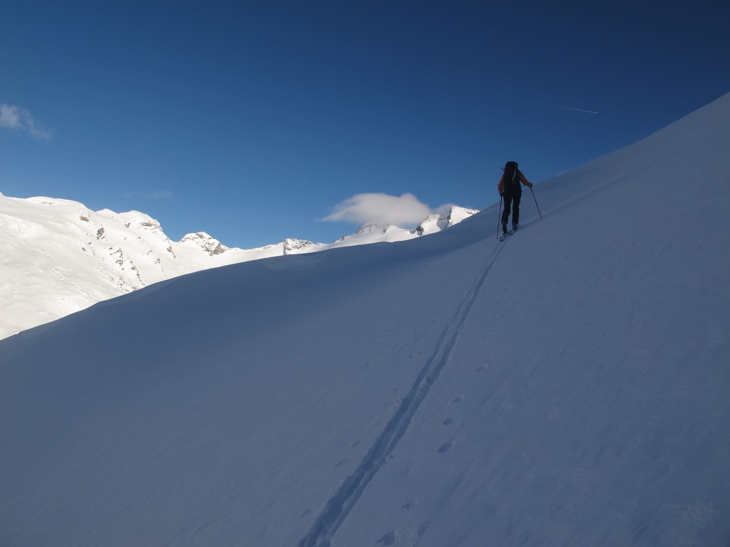 A lone ski tourer breaking trail up a clean snow ridge