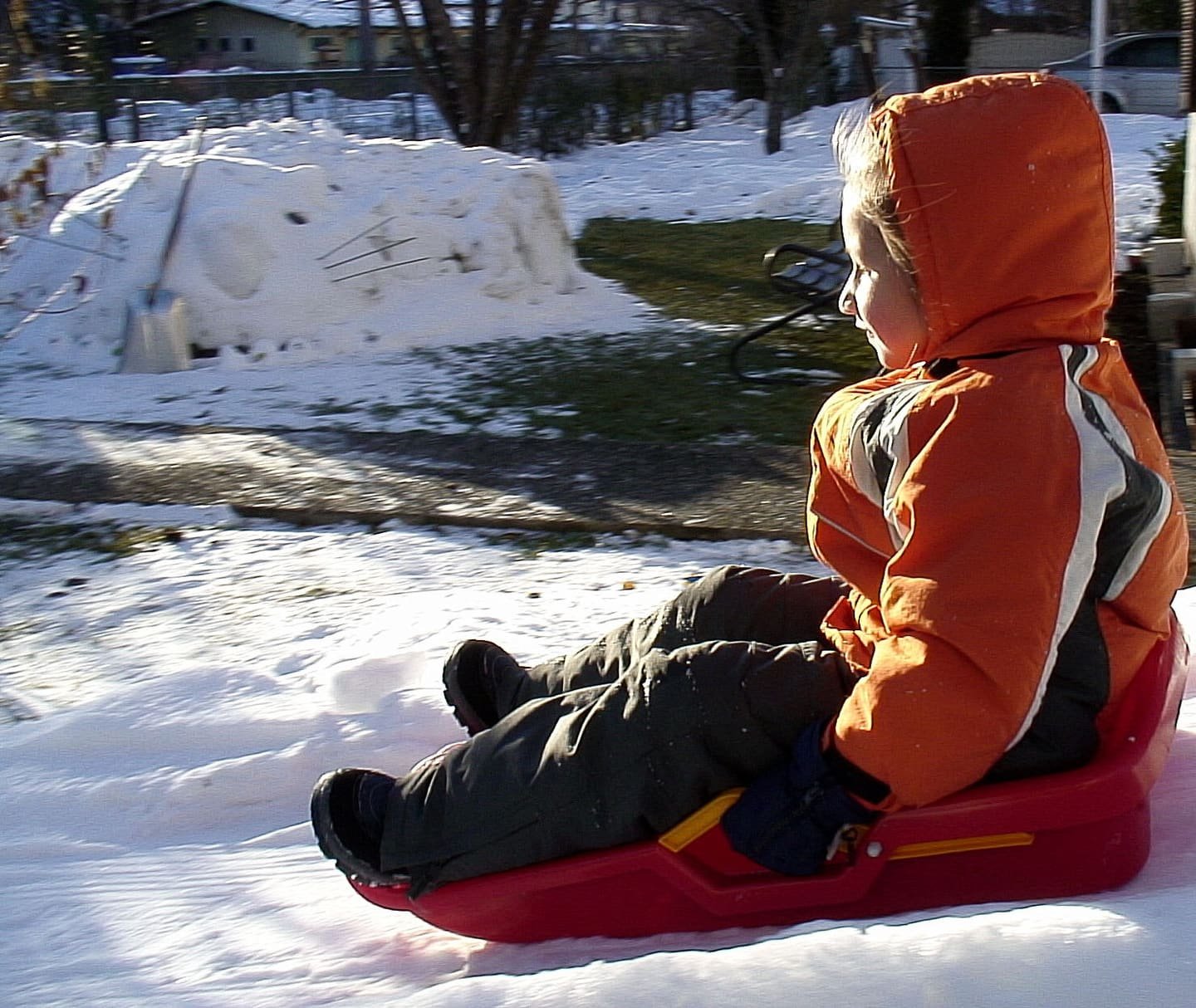 Un bambino con la tuta da neve seduto su uno slittino